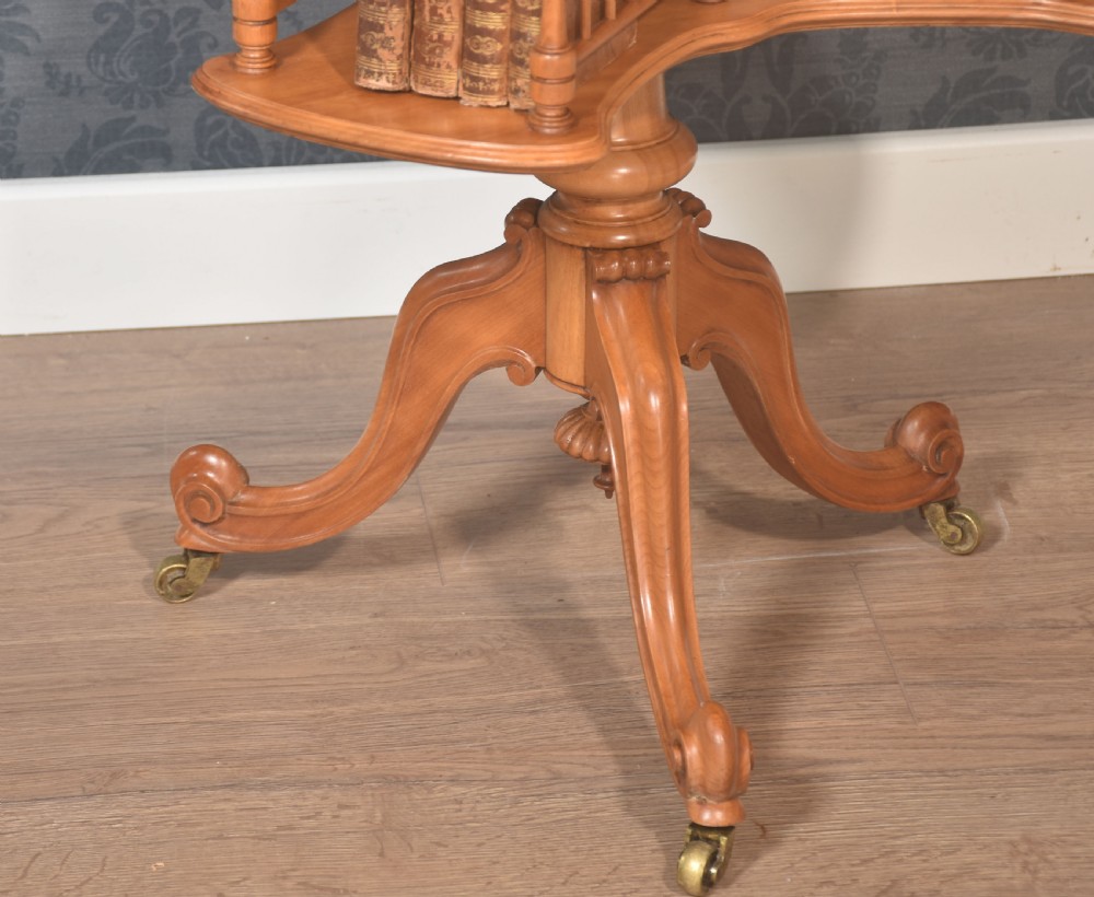 A satinwood revolving book table featuring a flat rectangular top, a rotating lower shelf with spindled galleries, and a tripod base on brass castors. View III