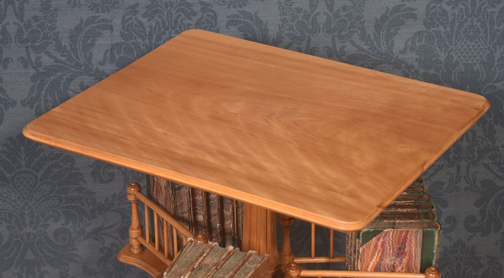 A satinwood revolving book table featuring a flat rectangular top, a rotating lower shelf with spindled galleries, and a tripod base on brass castors. View VI