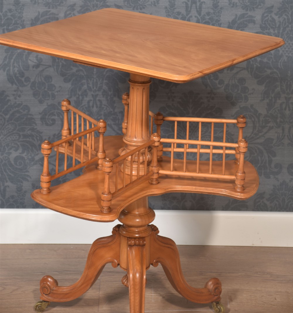 A satinwood revolving book table featuring a flat rectangular top, a rotating lower shelf with spindled galleries, and a tripod base on brass castors. View VIII