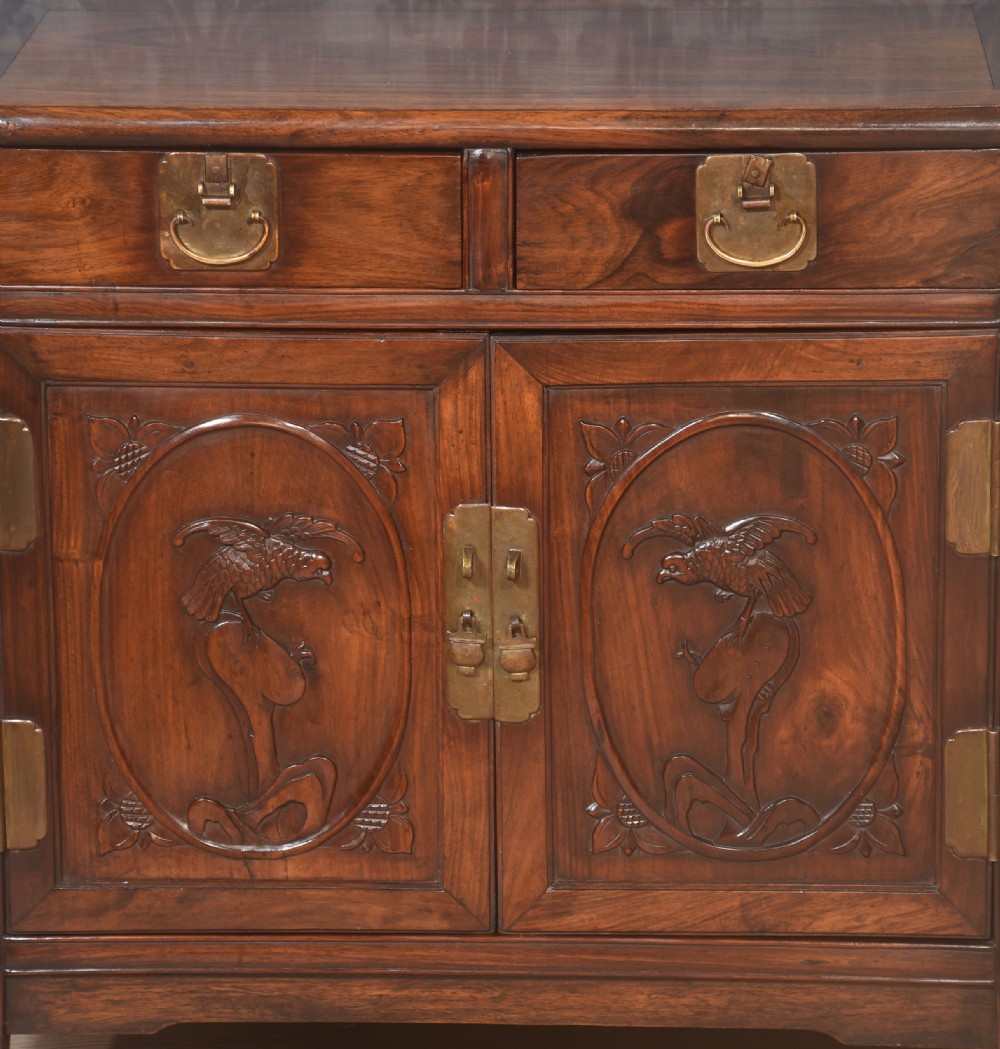 A warm brown carved Chinese wooden cupboard featuring two top drawers, brass hardware, and panelled doors depicting bird motifs. View II