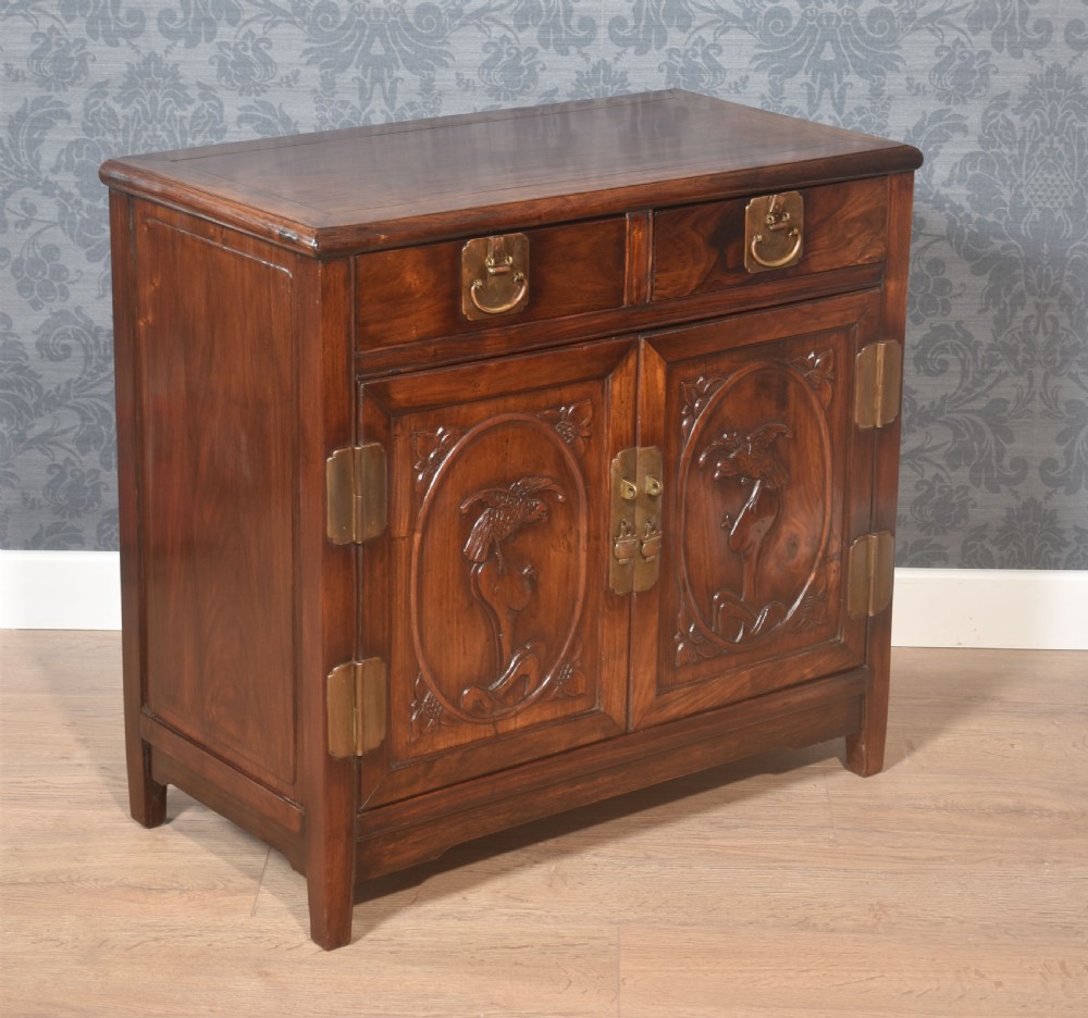 A warm brown carved Chinese wooden cupboard featuring two top drawers, brass hardware, and panelled doors depicting bird motifs. View V