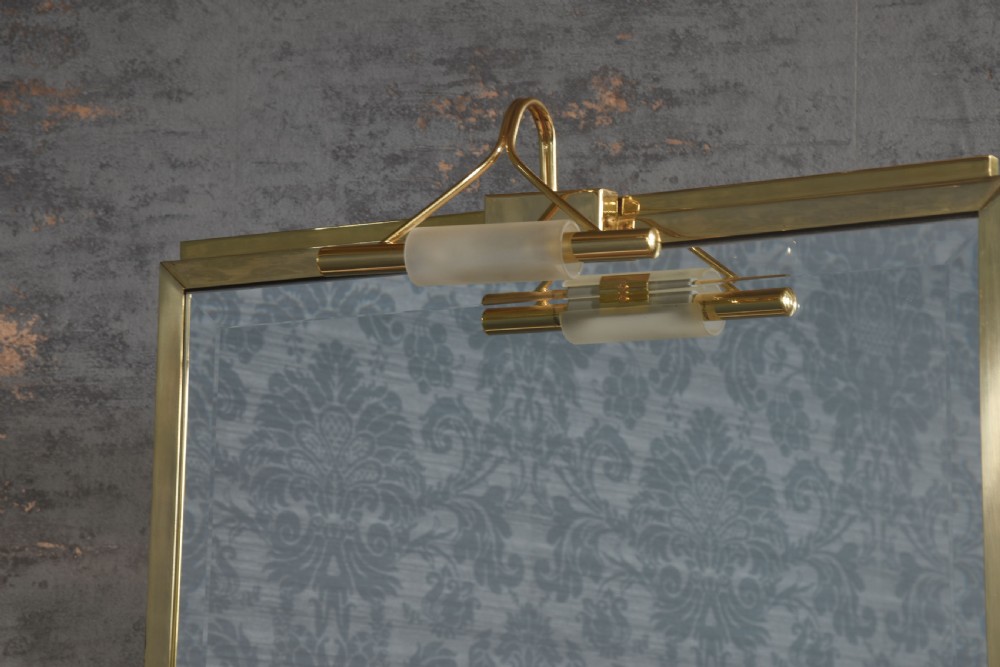 A full-length double-sided freestanding dressing mirror featuring a polished brass frame with an integrated top light fixture, mounted on dark wood supports with a brass Greek key motif at the base. View II