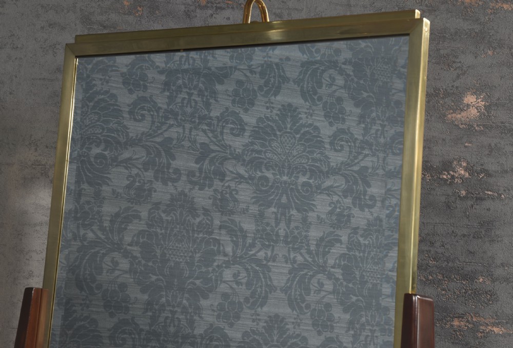 A full-length double-sided freestanding dressing mirror featuring a polished brass frame with an integrated top light fixture, mounted on dark wood supports with a brass Greek key motif at the base. View V