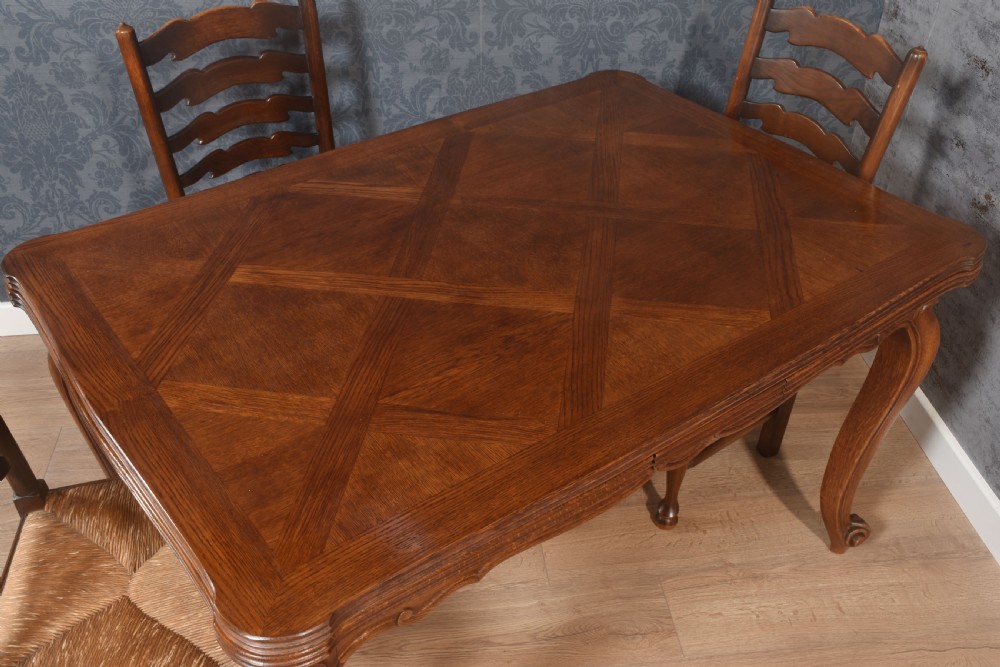 A French oak dining table featuring a geometric parquetry top, shaped apron, cabriole legs, and a draw-leaf extension mechanism. View III