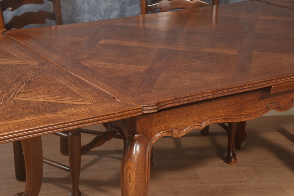 A French oak dining table featuring a geometric parquetry top, shaped apron, cabriole legs, and a draw-leaf extension mechanism. View V