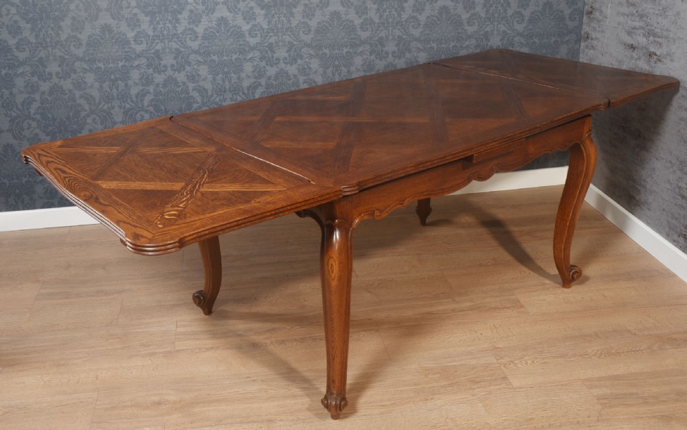 A French oak dining table featuring a geometric parquetry top, shaped apron, cabriole legs, and a draw-leaf extension mechanism. View VII
