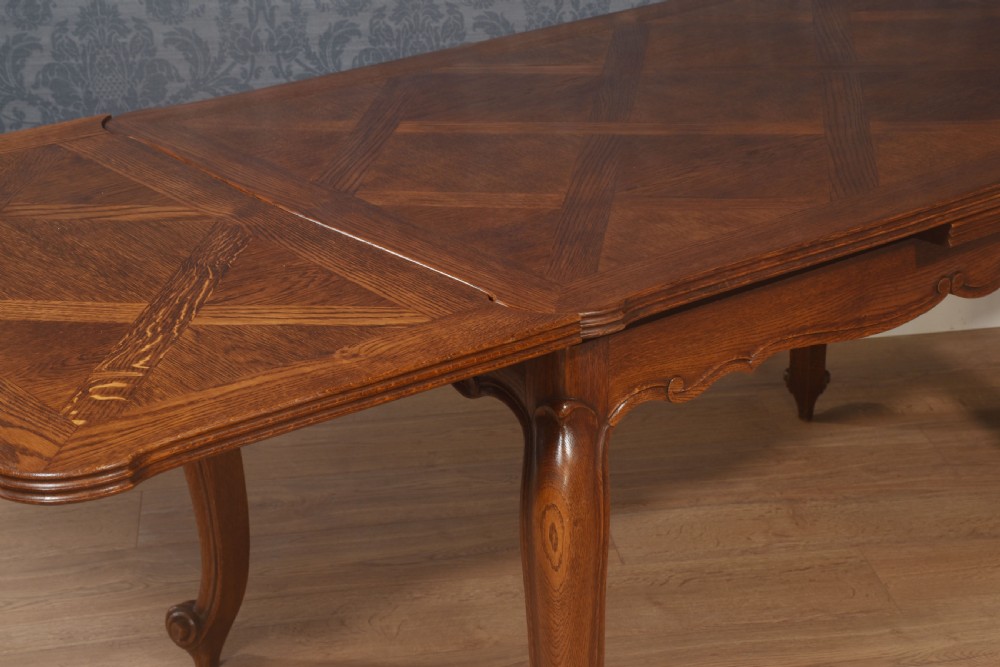 A French oak dining table featuring a geometric parquetry top, shaped apron, cabriole legs, and a draw-leaf extension mechanism. View VIII
