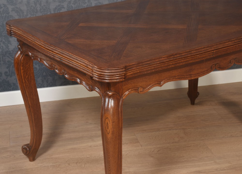 A French oak dining table featuring a geometric parquetry top, shaped apron, cabriole legs, and a draw-leaf extension mechanism. View IX