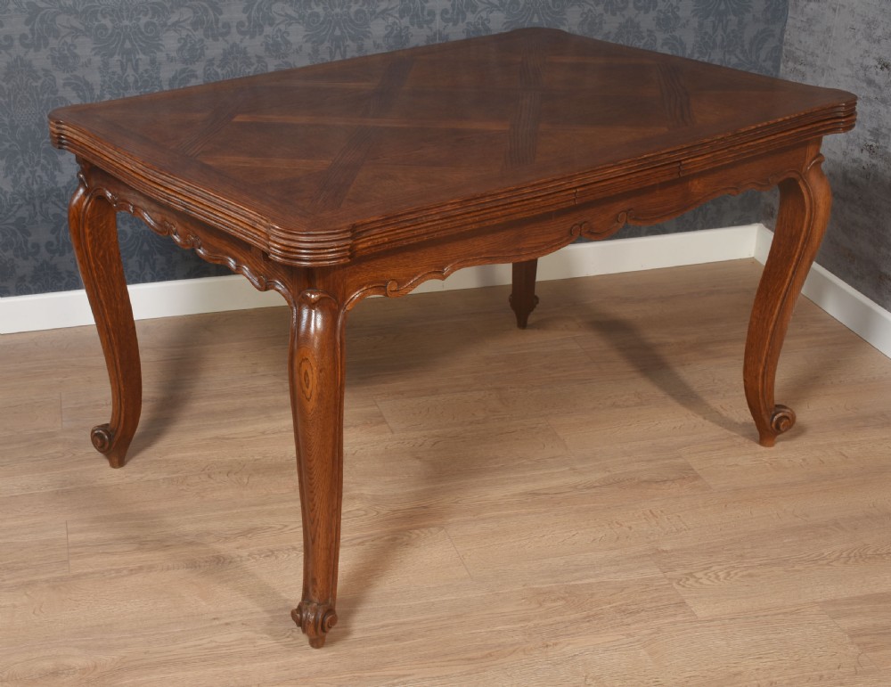A French oak dining table featuring a geometric parquetry top, shaped apron, cabriole legs, and a draw-leaf extension mechanism. View X