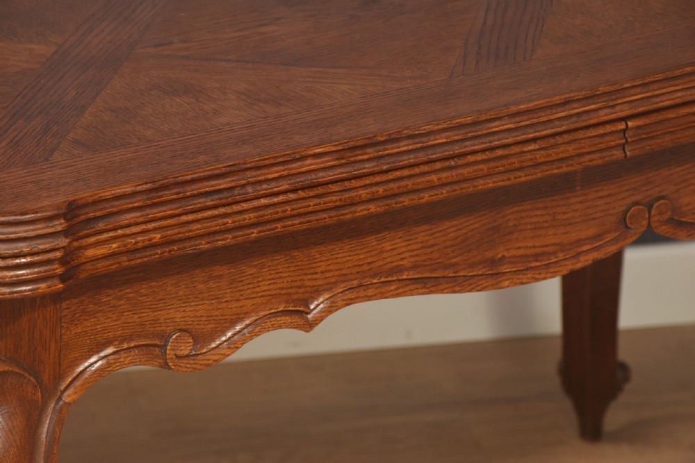 A French oak dining table featuring a geometric parquetry top, shaped apron, cabriole legs, and a draw-leaf extension mechanism. View XII