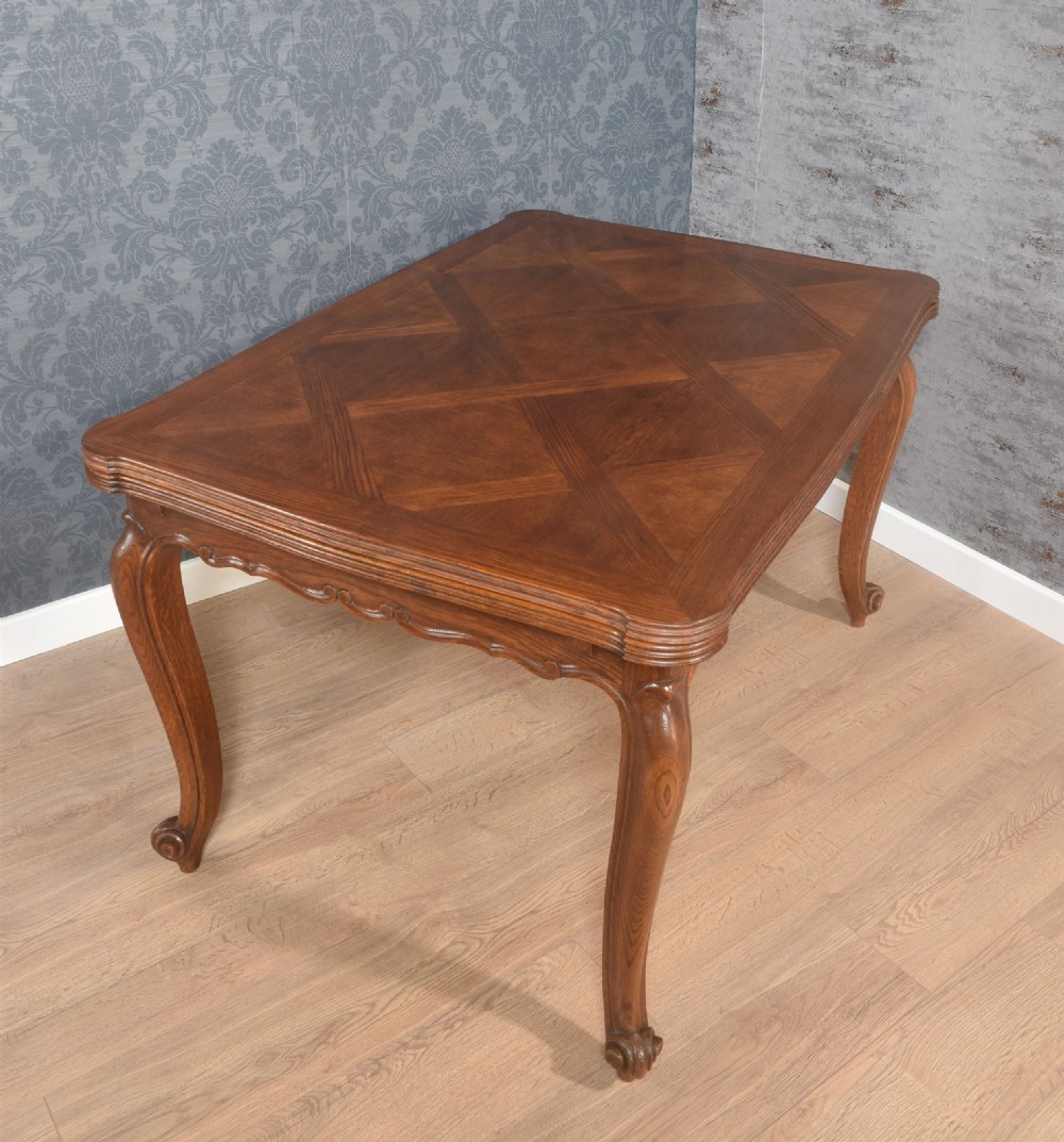 A French oak dining table featuring a geometric parquetry top, shaped apron, cabriole legs, and a draw-leaf extension mechanism. View XIII