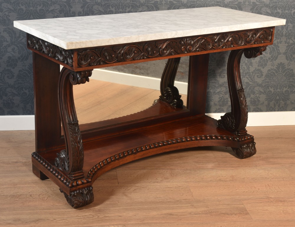 A 19th-century mahogany console table with a rectangular white marble top, carved frieze, S-shaped scroll supports, and an inset mirror back above a shaped plinth base.
