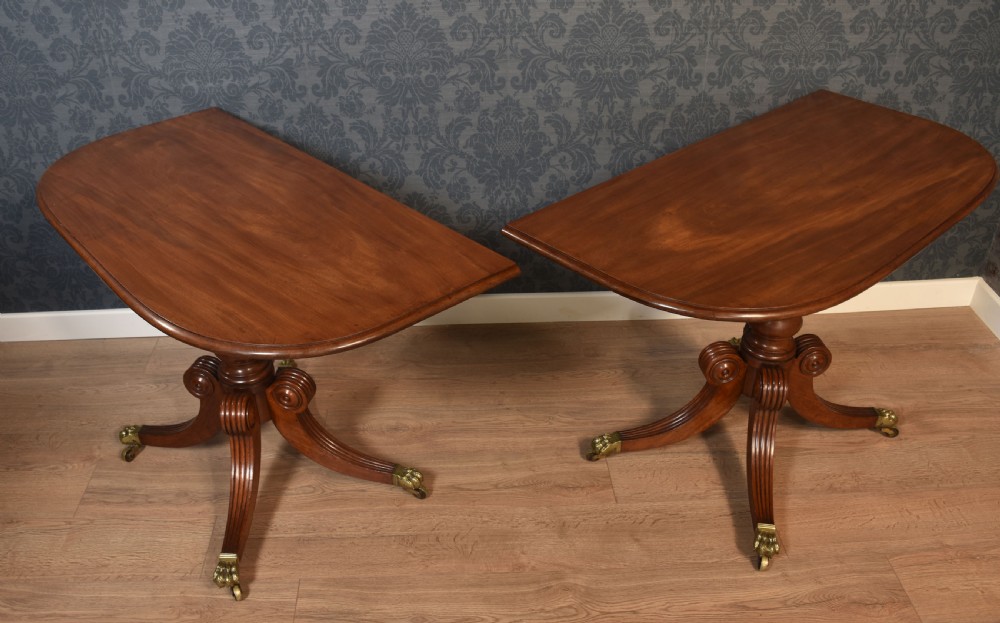 A pair of Regency mahogany semi-oval hall tables on reeded pedestal legs with brass claw feet.