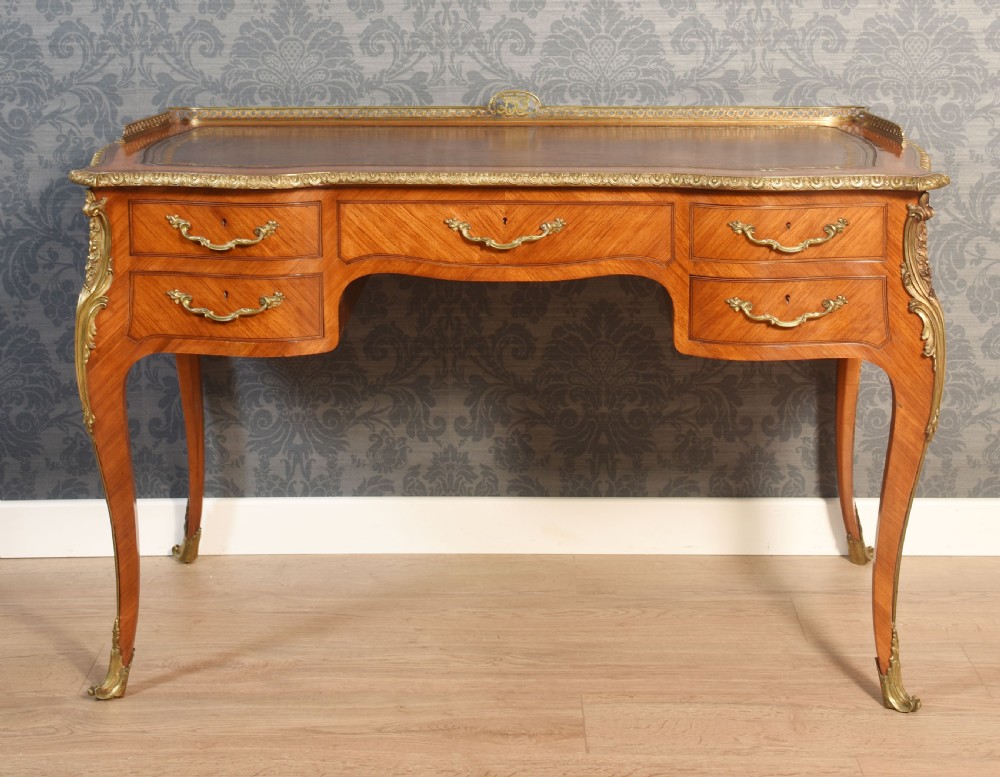 A 19th-century kingwood writing table featuring five drawers, ornate ormolu mounts, cabriole legs, and a leather-inset writing surface.