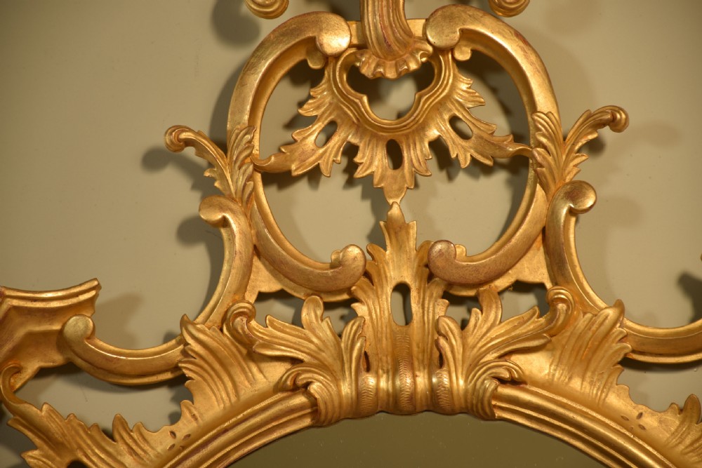 An ornate oval wall mirror featuring an intricately carved giltwood frame decorated with scrolling acanthus leaves and a pierced crest. View VII