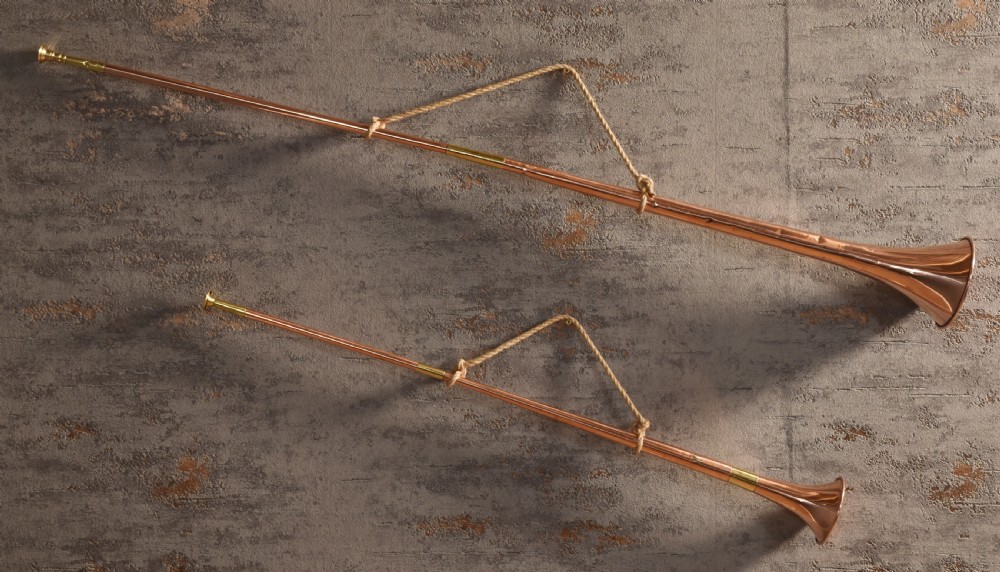 A set of two straight copper coaching horns with brass mouthpieces and flared bells, each rigged with a suspension rope.