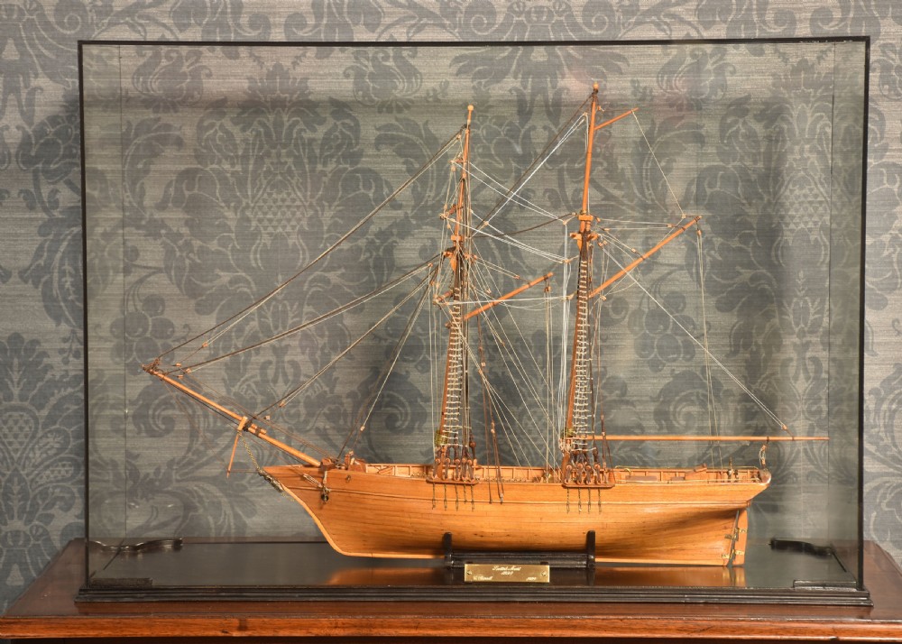 A detailed wooden scale model of a two-masted Scottish schooner with intricate thread rigging, displayed inside a clear glass case with a brass plaque.