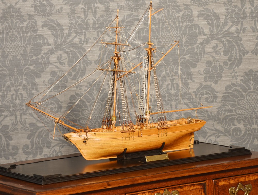 A detailed wooden scale model of a two-masted Scottish schooner with intricate thread rigging, displayed inside a clear glass case with a brass plaque. View V