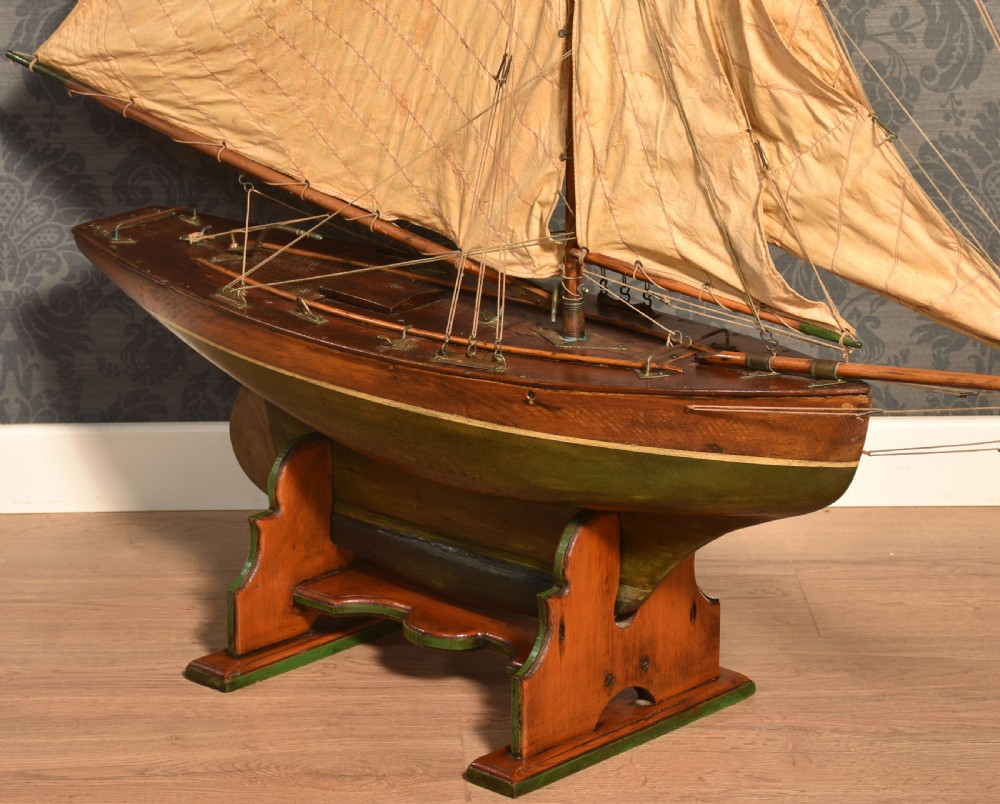 A 19th-century wooden pond yacht featuring cream canvas sails, a carved brown hull with green painted keel accents, and a wooden display stand. View VIII