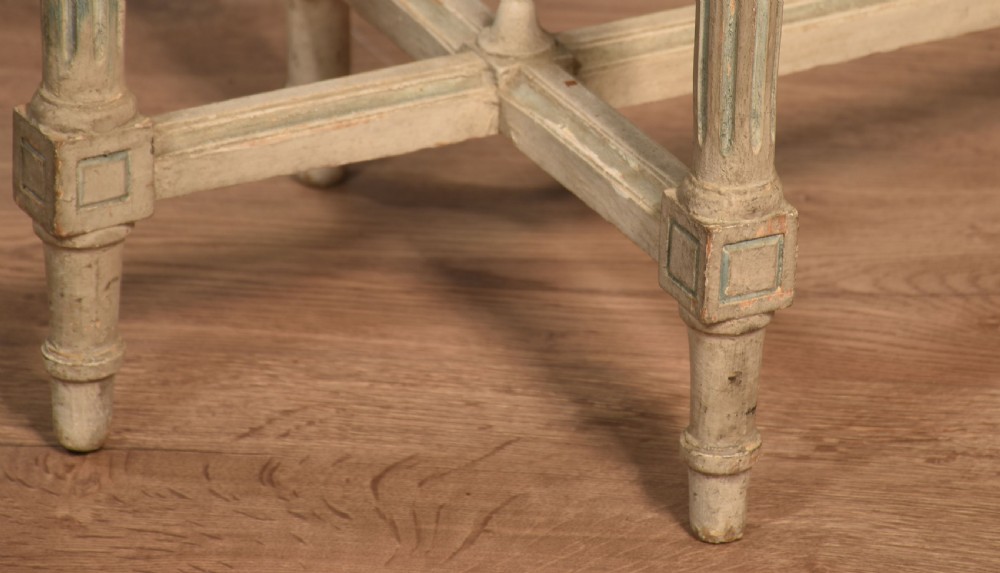 An oval window seat featuring a woven cane top set within a painted off-white wooden frame with fluted turned legs and carved rosettes. View VIII