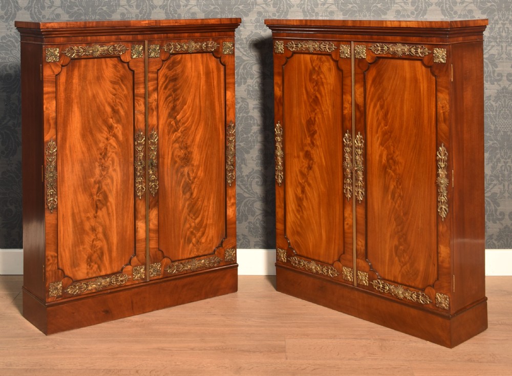 A matching pair of low mahogany side cabinets featuring double panel doors with figured flame grain and decorative gilt metal mounts.
