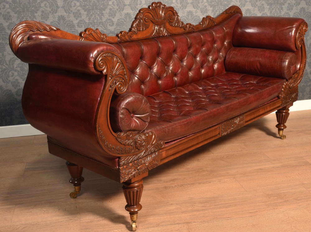 An early 19th-century deep-buttoned burgundy leather scroll-end settee with a carved mahogany frame, bolster cushions, and turned legs on brass castors. View XII