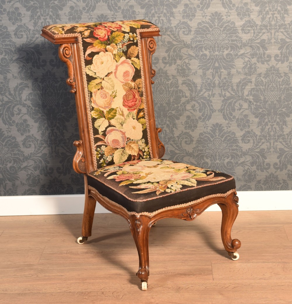 A Victorian high-backed nursing chair featuring a carved walnut frame, cabriole front legs on castors, and floral tapestry upholstery.