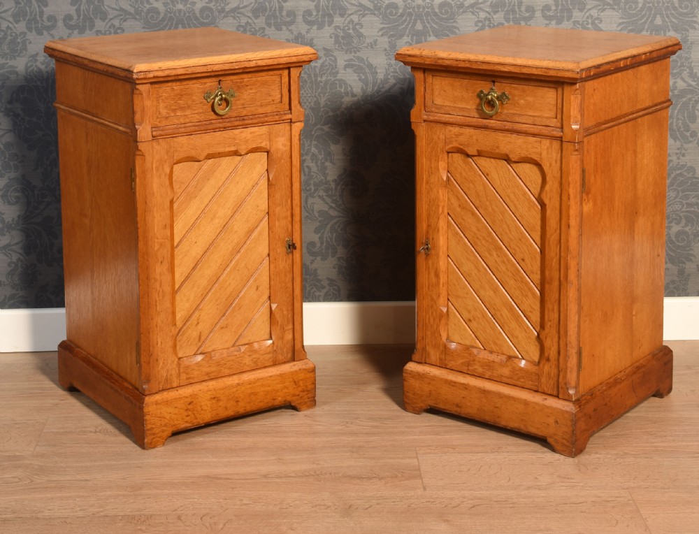 A matching pair of golden oak bedside cabinets featuring single top drawers with brass ring pulls and lower cupboard doors with diagonal plank detailing.