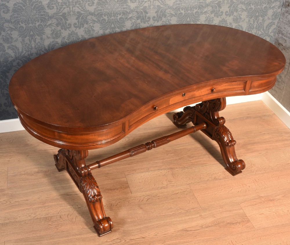 A Victorian mahogany kidney-shaped desk featuring carved trestle legs, a turned stretcher, and a single frieze drawer.