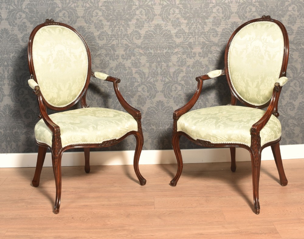 A pair of antique mahogany open armchairs featuring oval backrests, cabriole legs, and pale sage green damask upholstery.