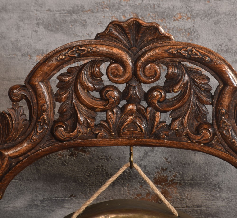A free-standing carved dark oak dinner gong featuring barley twist columns, intricate scroll cresting, a suspended circular brass disc, and a leather striker. View IV