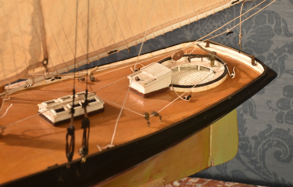 A detailed wooden model of a twin-masted racing yacht with cream canvas sails, a painted black upper hull, and a natural wood display stand. View IX