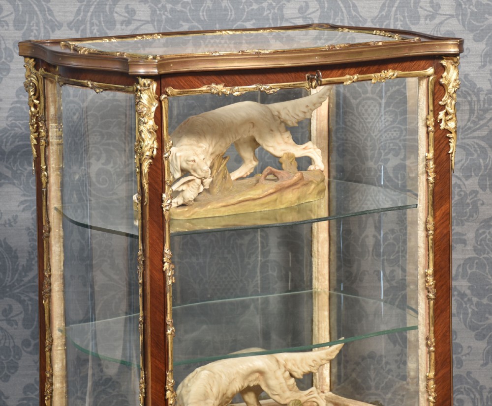 A French walnut vitrine display cabinet featuring glazed curved side panels, gilt-bronze ormolu mounts, glass shelves, and cabriole legs. View II