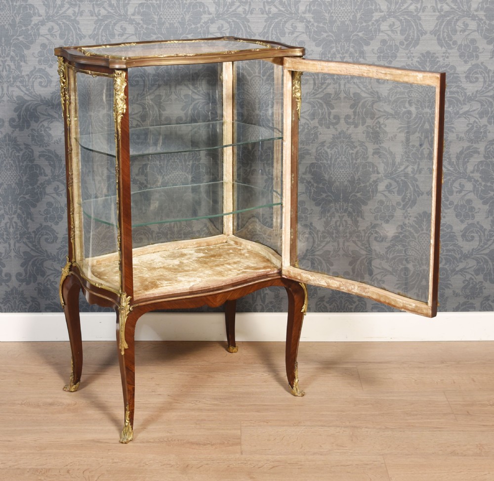 A French walnut vitrine display cabinet featuring glazed curved side panels, gilt-bronze ormolu mounts, glass shelves, and cabriole legs. View VII