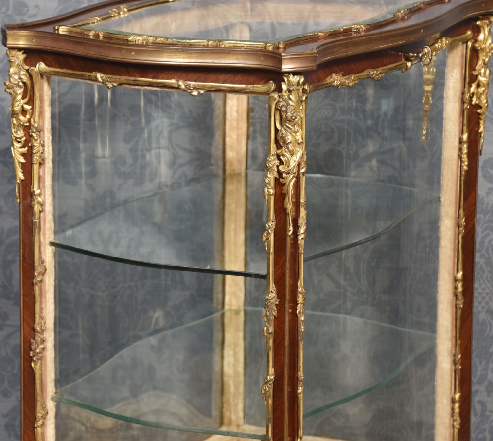A French walnut vitrine display cabinet featuring glazed curved side panels, gilt-bronze ormolu mounts, glass shelves, and cabriole legs. View XII