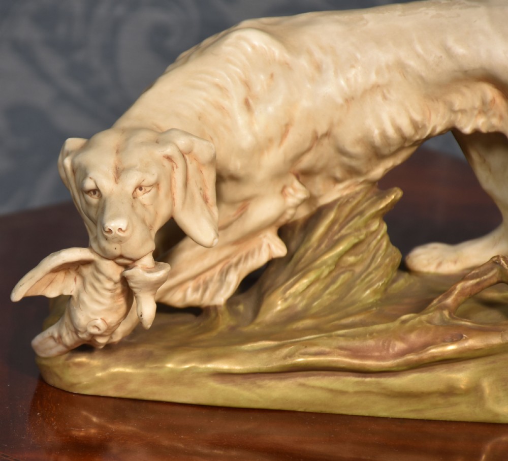 An antique Royal Dux matt porcelain figurine depicting a setter dog holding a game bird on a foliage base. View II