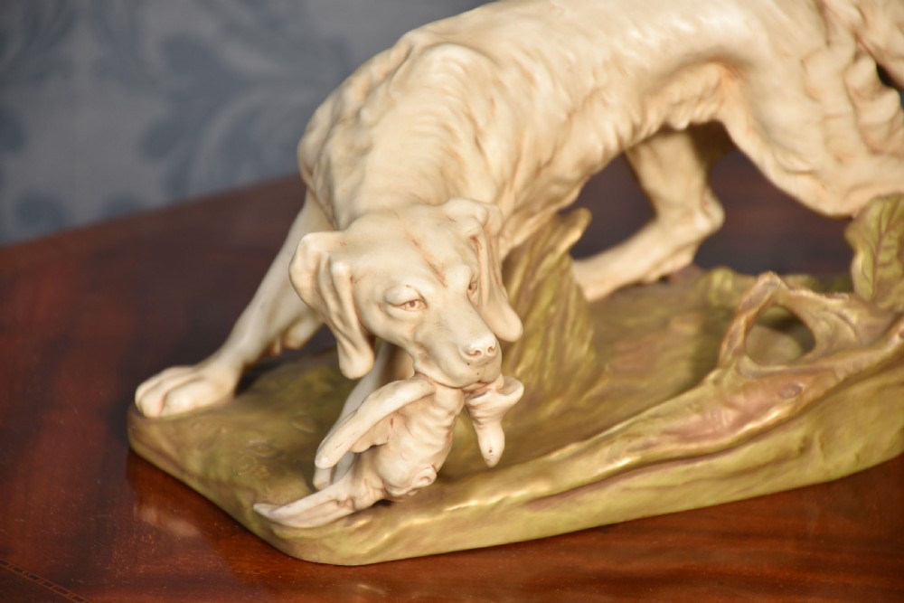 An antique Royal Dux matt porcelain figurine depicting a setter dog holding a game bird on a foliage base. View III