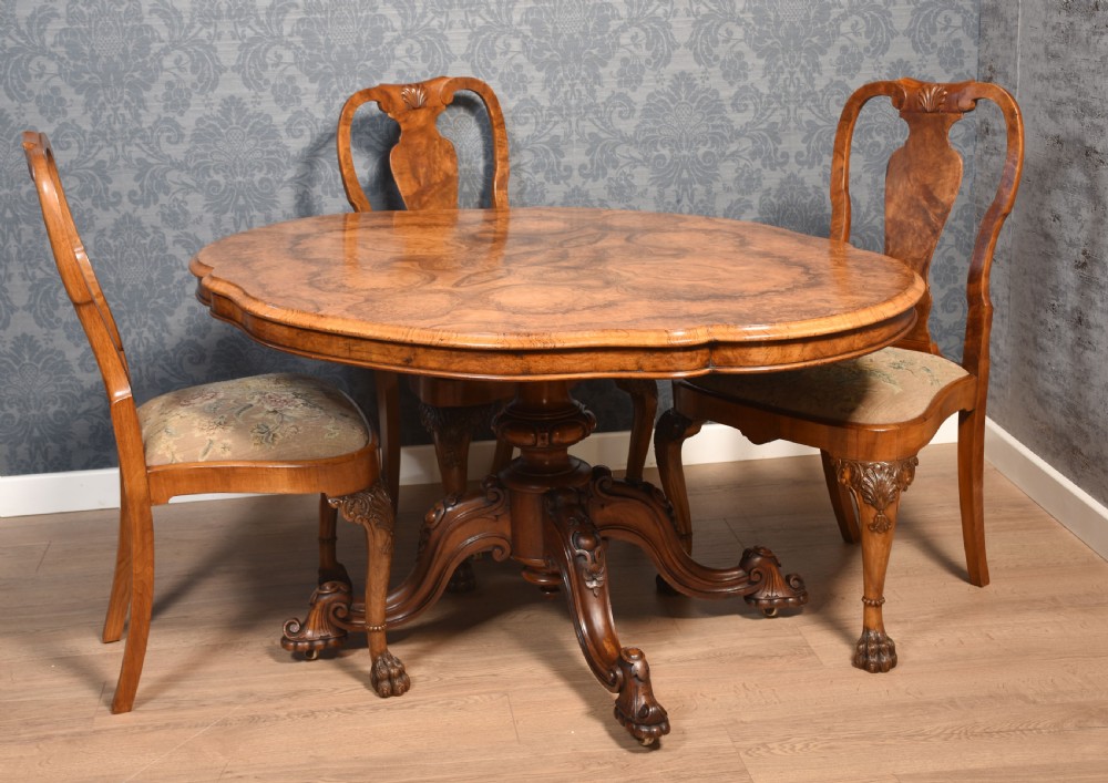 A Victorian oval burr walnut centre table with a shaped edge, turned central pedestal, and four ornate scroll-carved legs on brass castors. View II