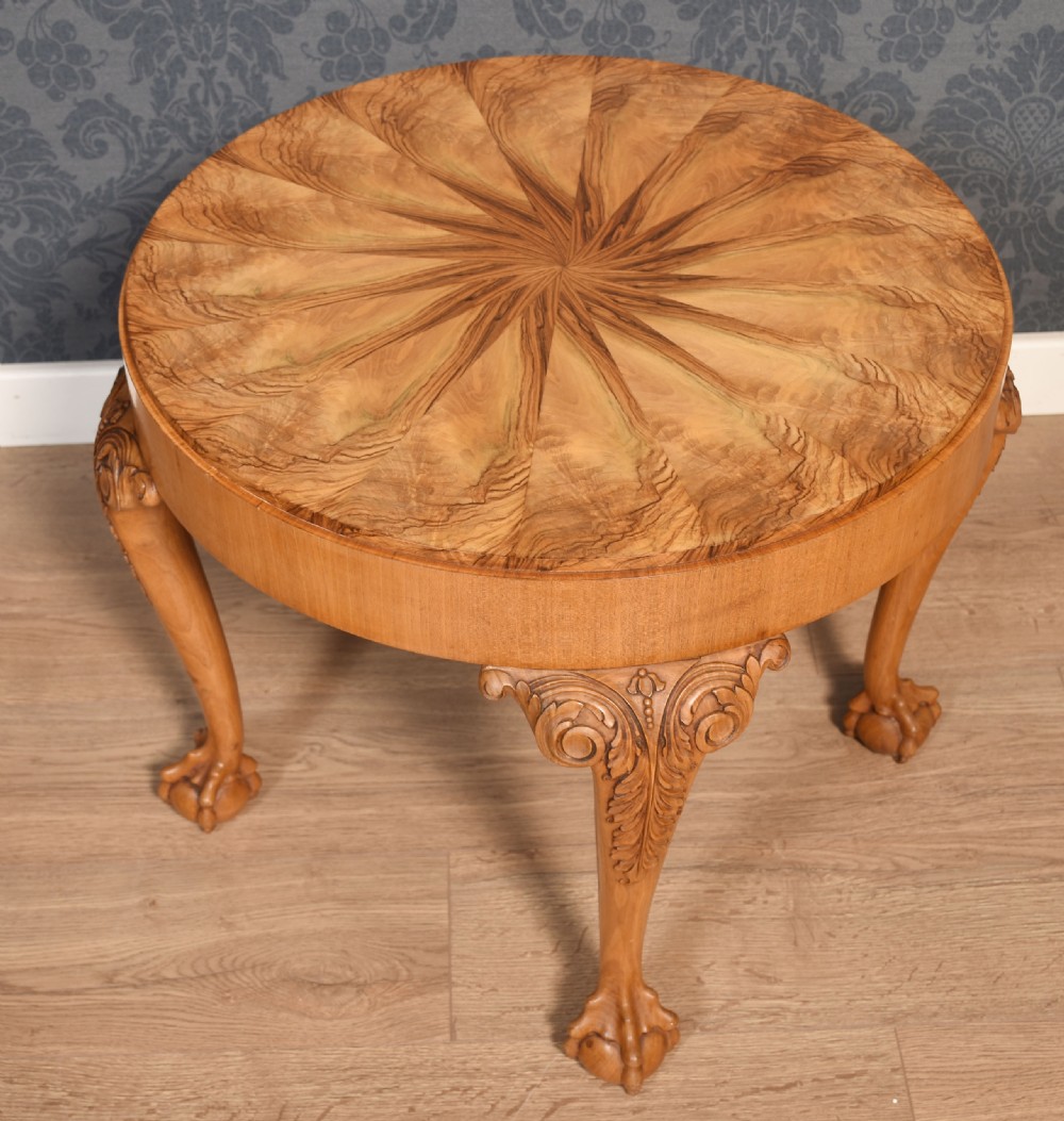 A circular low coffee table featuring a starburst burr walnut veneered top, carved cabriole legs with leaf details, and ball-and-claw feet.