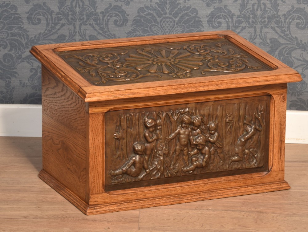 A Victorian slant-front oak slipper box featuring relief-embossed copper panels with cherubs on the front and a floral motif on the lid.