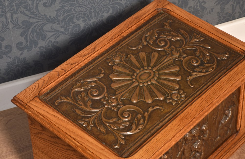 A Victorian slant-front oak slipper box featuring relief-embossed copper panels with cherubs on the front and a floral motif on the lid. View V