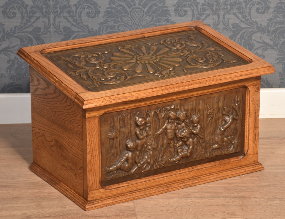 A Victorian slant-front oak slipper box featuring relief-embossed copper panels with cherubs on the front and a floral motif on the lid. View VI
