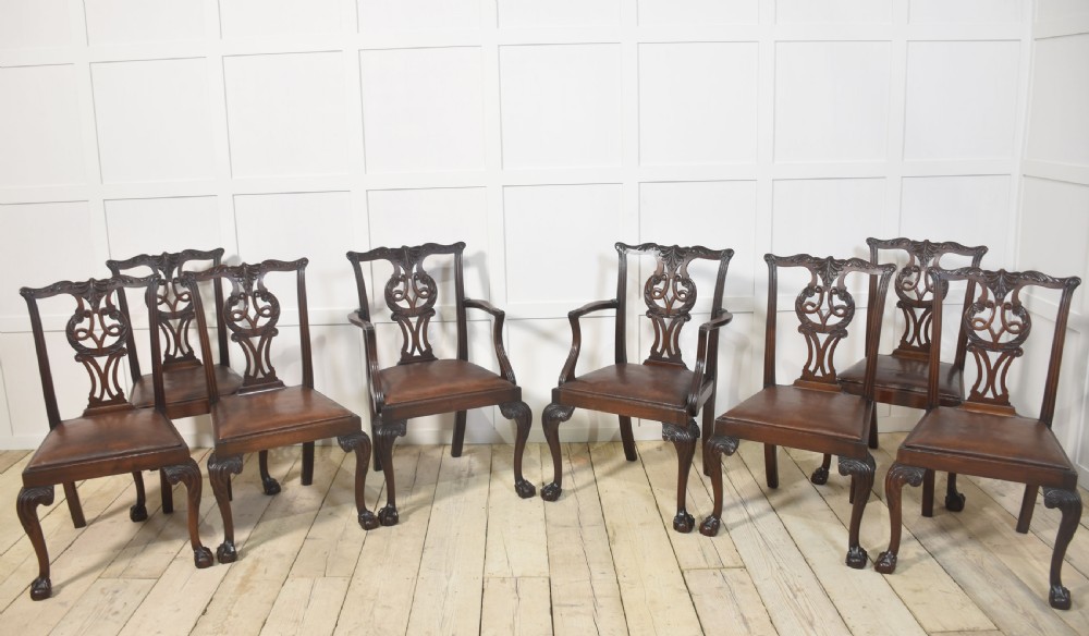 A set of eight mahogany Chippendale style dining chairs with carved splats, leather seats, and cabriole legs with ball-and-claw feet.