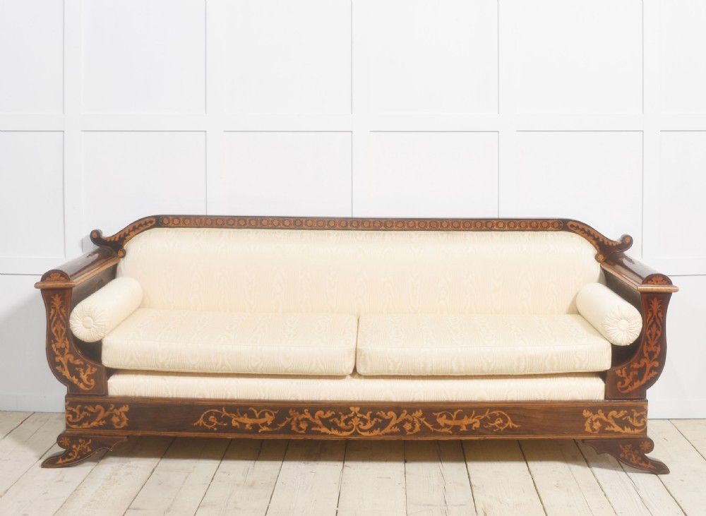 A Dutch marquetry settee with dark wood floral inlay along the frame and light cream upholstered cushions.