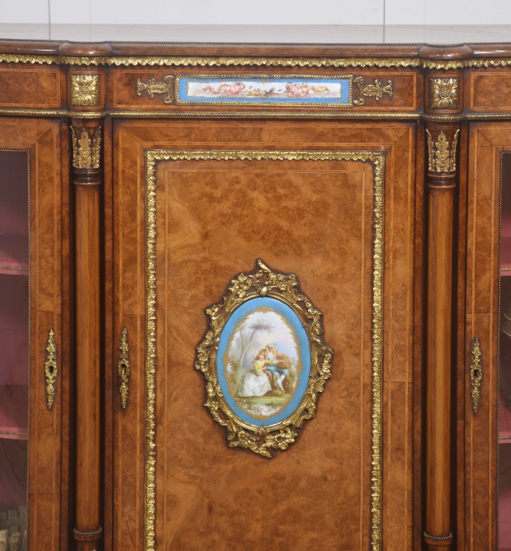 A Victorian burr walnut credenza featuring a central solid cupboard door with a porcelain plaque flanked by two bowed glazed side doors and gilt metal mounts. View III