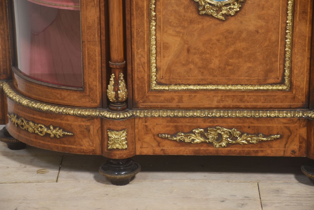 A Victorian burr walnut credenza featuring a central solid cupboard door with a porcelain plaque flanked by two bowed glazed side doors and gilt metal mounts. View VIII