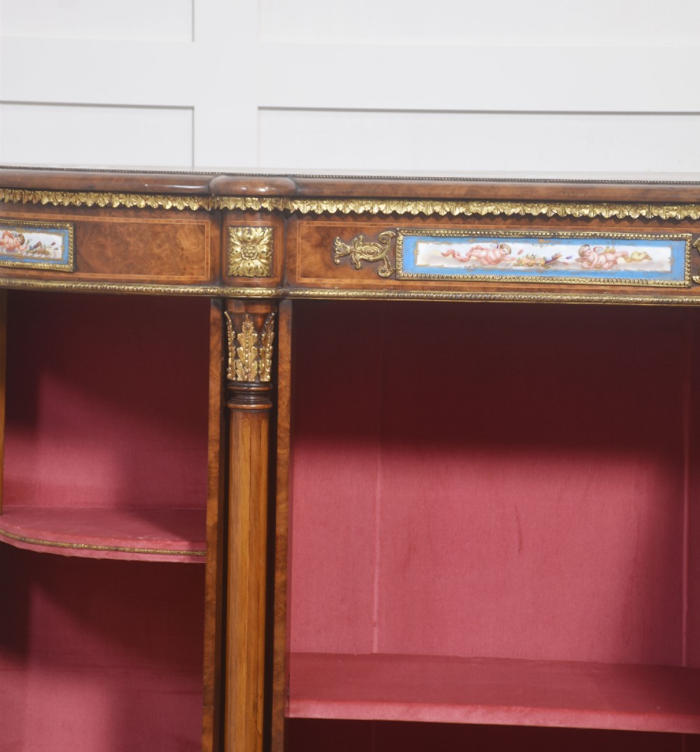 A Victorian burr walnut credenza featuring a central solid cupboard door with a porcelain plaque flanked by two bowed glazed side doors and gilt metal mounts. View XII