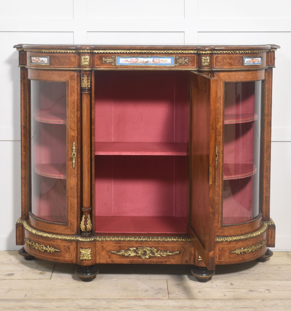 A Victorian burr walnut credenza featuring a central solid cupboard door with a porcelain plaque flanked by two bowed glazed side doors and gilt metal mounts. View XIII