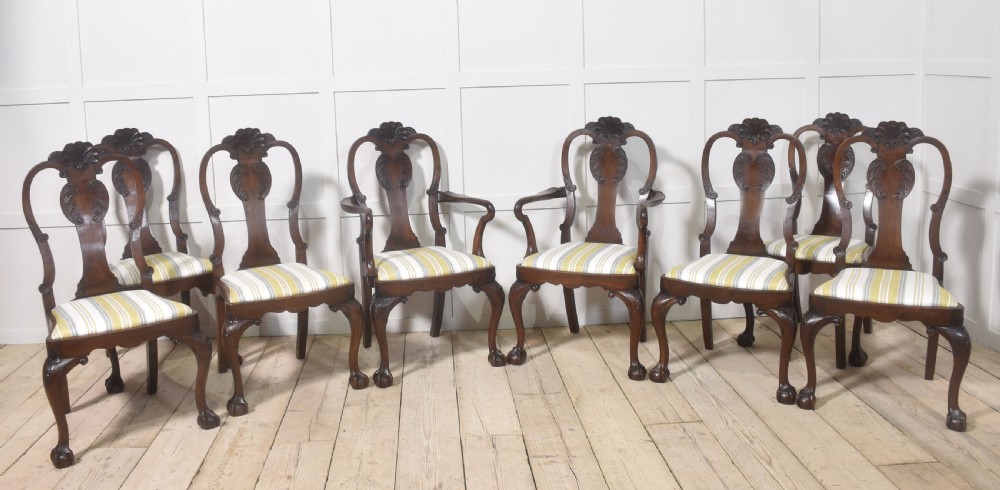 A set of eight carved dark walnut dining chairs with shell cresting rails, cabriole legs, ball-and-claw feet, and striped upholstered seat pads.