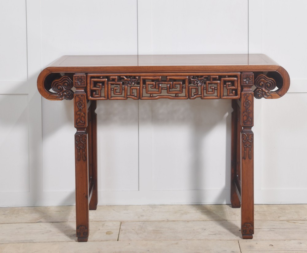A Chinese carved hardwood altar table featuring upturned everted flanges, geometric openwork fretwork along the apron, and carved square legs.